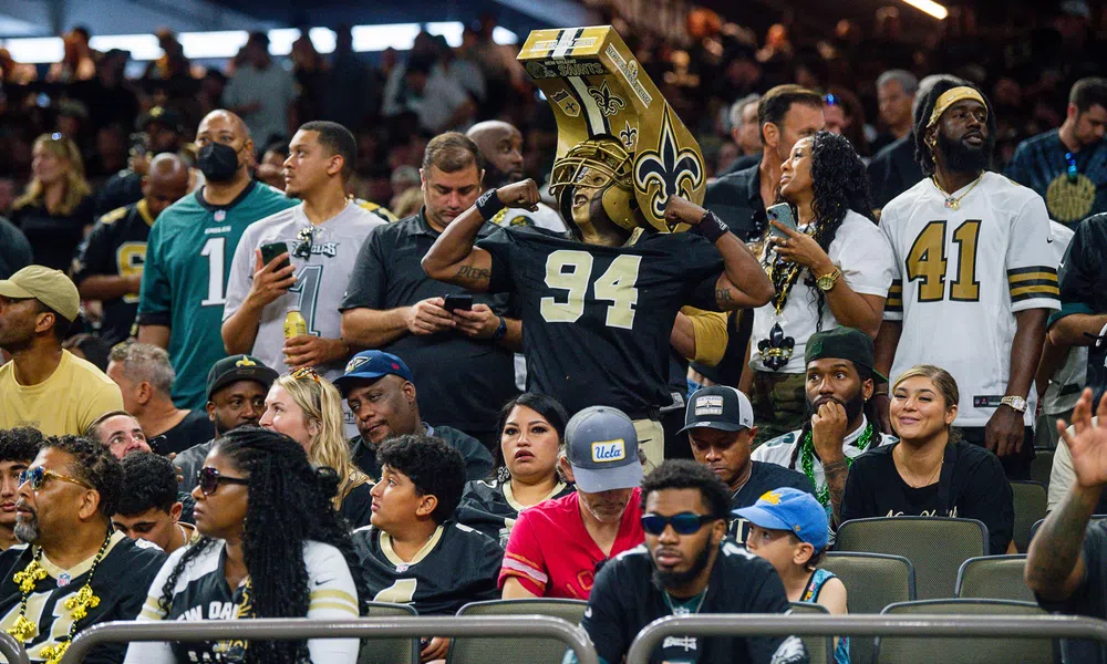 Excited fans at football game, some wearing New Orleans Saints jerseys and merchandise in stadium seats.