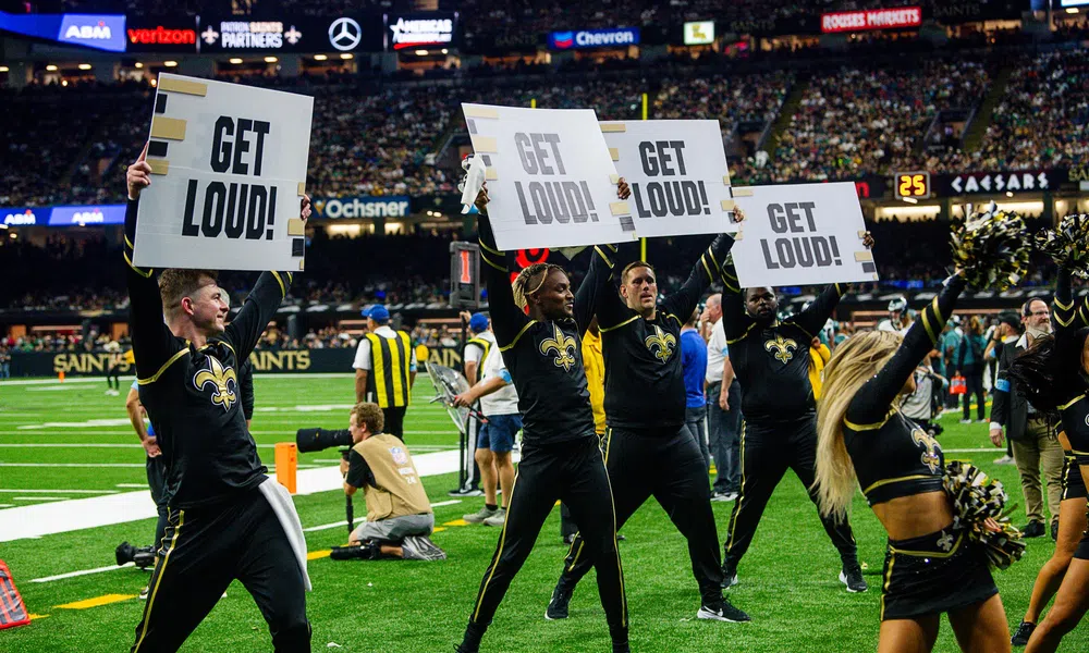 New Orleans Saints cheerleaders and dancers holding Get Loud signs on the football field during a game.