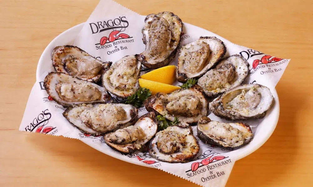 Grilled oysters on a white plate with lemon wedges, served on branded paper from Drago's Seafood Restaurant.