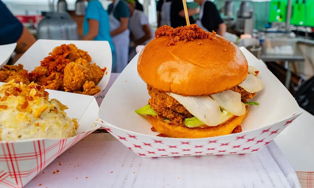 Crispy fried chicken sandwich with lettuce and sauce in a paper tray at a food market stall.