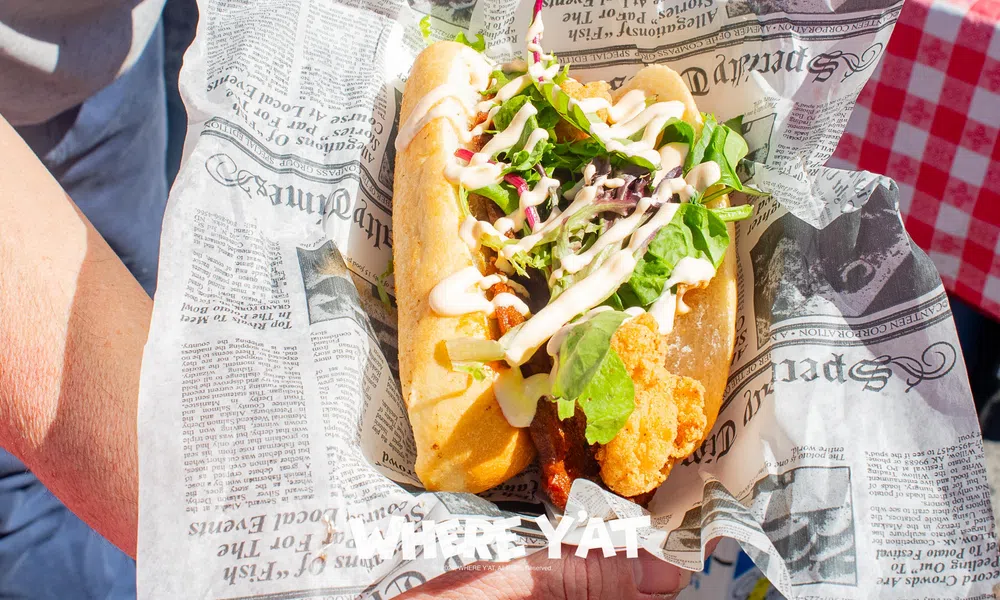 Fresh fried fish sandwich with lettuce and sauce served in newspaper-style wrapping held by a person.