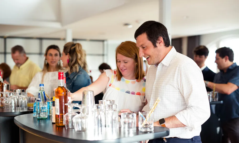 People enjoying drinks and socializing around a modern bar counter with bottles and glasses.