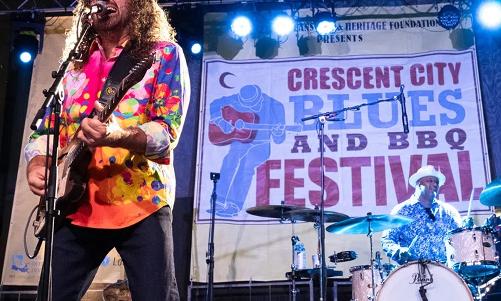 Singer with colorful shirt plays guitar and vocalist performs at Crescent City Blues and BBQ Festival concert.