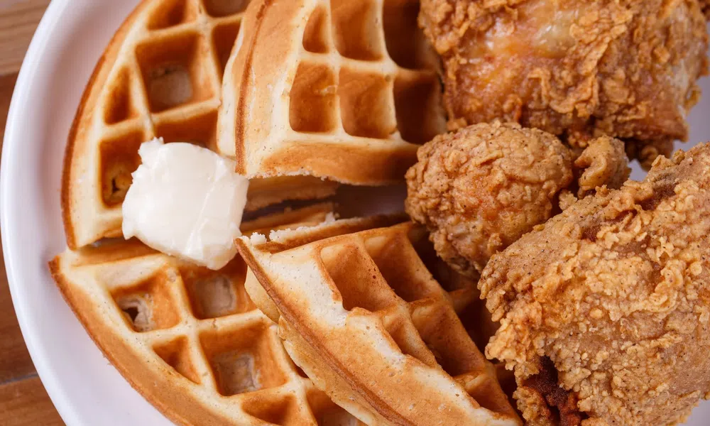 Crispy fried chicken pieces served with golden waffles and a dollop of melting butter on a white plate.