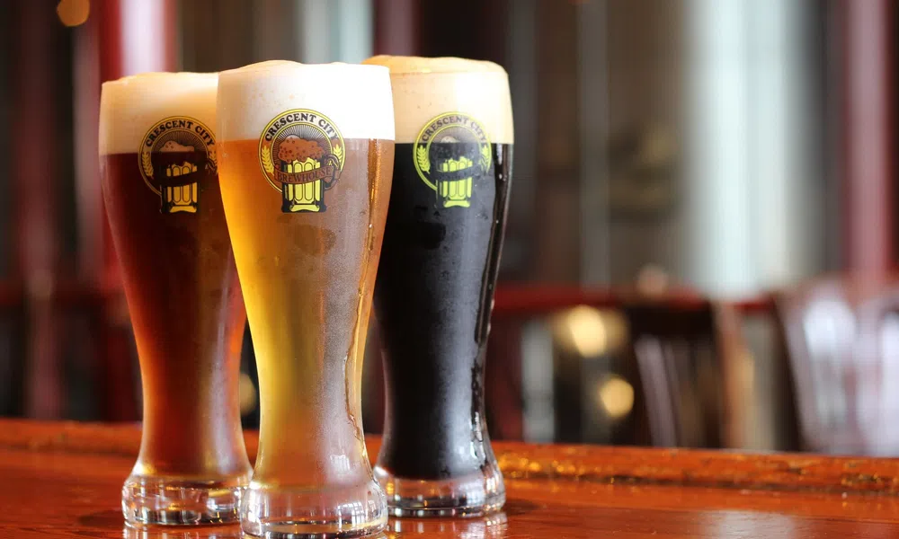 Three tall glasses of beer with varying colors and foam on a wooden bar counter in a pub setting.