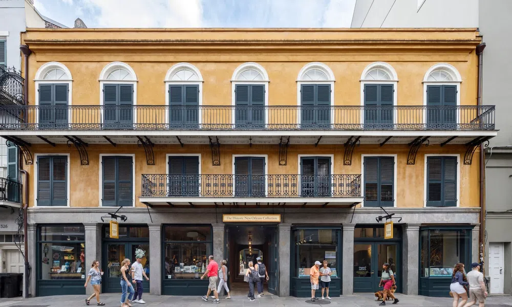 Historic yellow building with black shutters and iron balconies in a lively urban street scene.