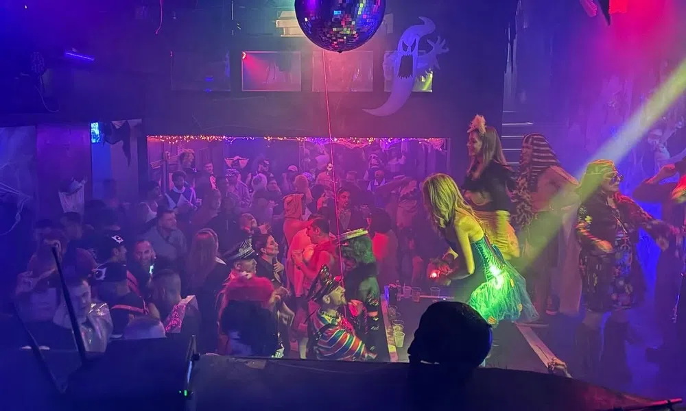 Crowded nightclub with people dancing and colorful lights under a large disco ball during a party