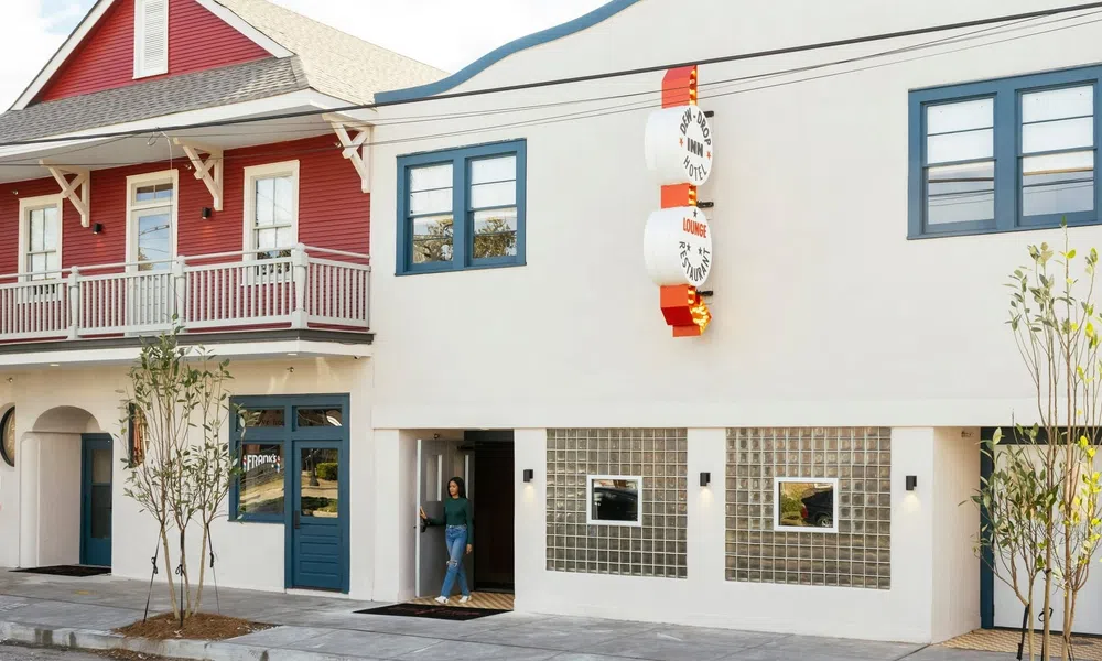Modern white building with blue accents and a red house with a balcony on the left side in a sunny street.