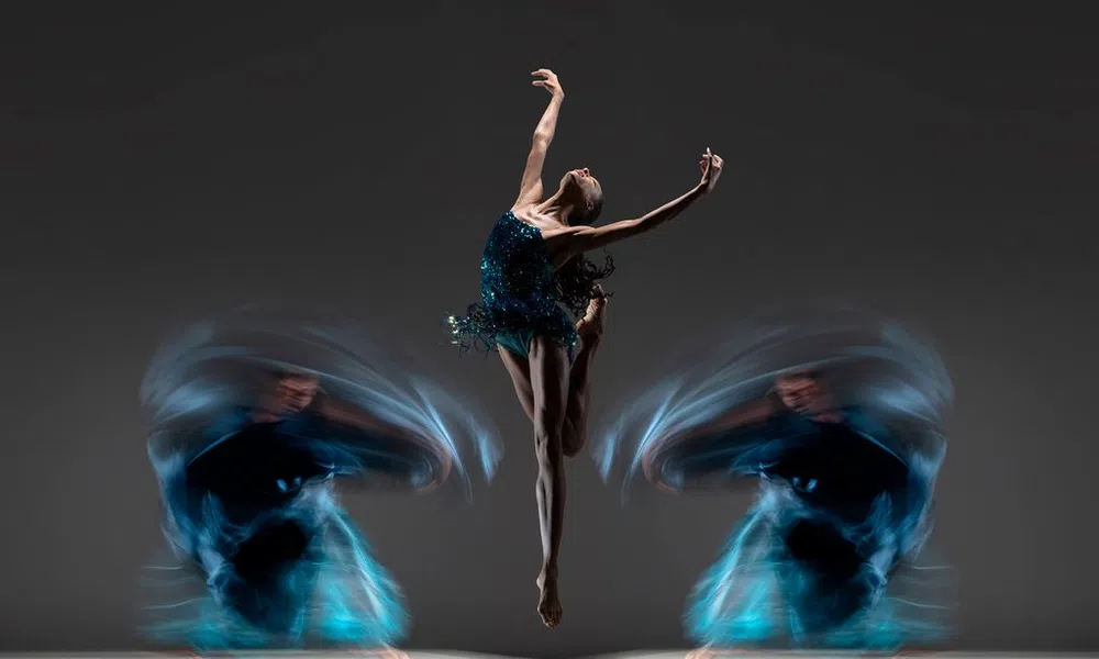 Ballet dancer in mid-air leap with blurred motion trails of dancers spinning on either side against dark background