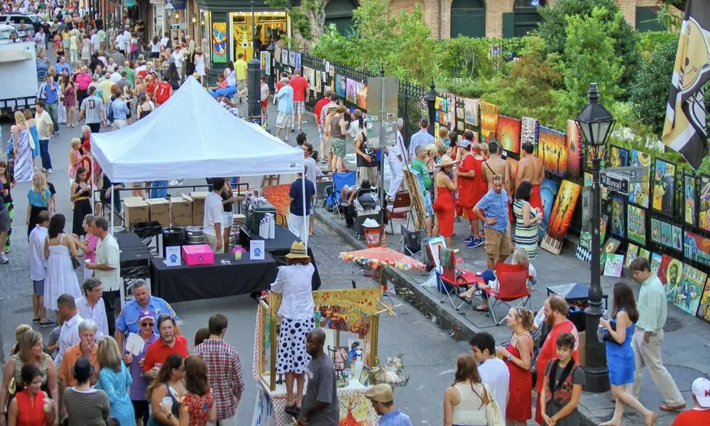 Outdoor art market with crowds browsing vibrant paintings displayed along a street on a sunny day