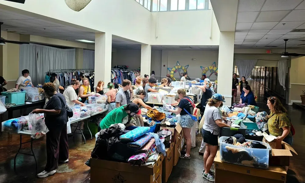 Volunteers sorting and organizing clothing donations in a large, well-lit community center with boxes and racks of clothes.