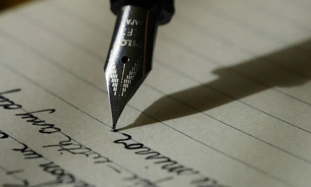 Close-up of a fountain pen writing cursive text on lined paper with shadow cast to the side