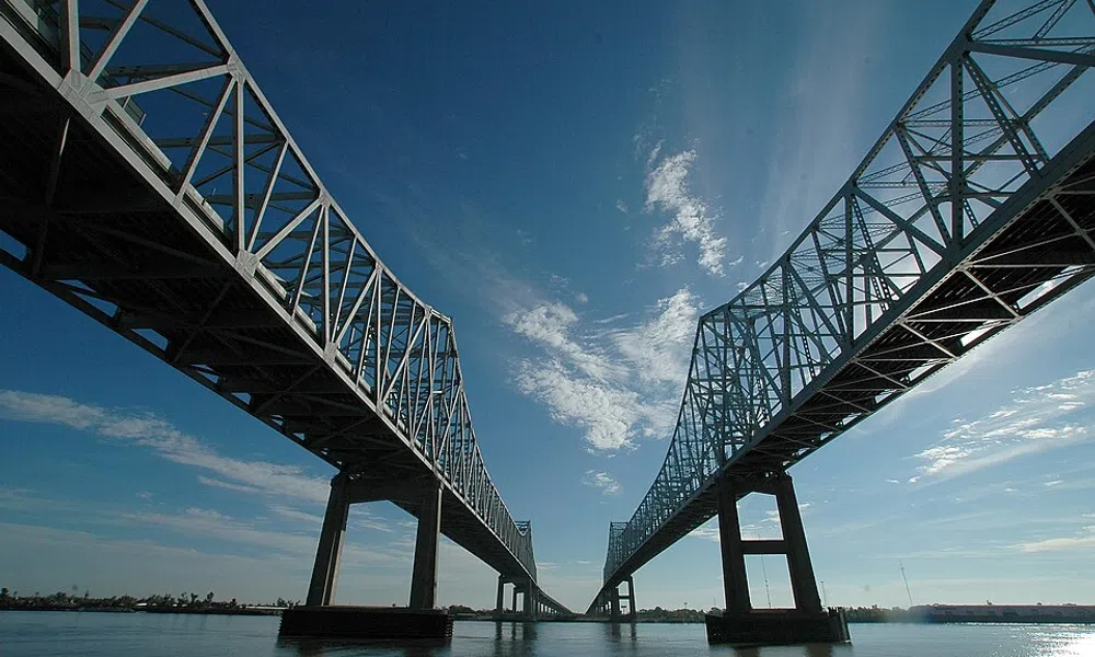 Steel truss bridge over calm river under blue sky with scattered white clouds on a sunny day