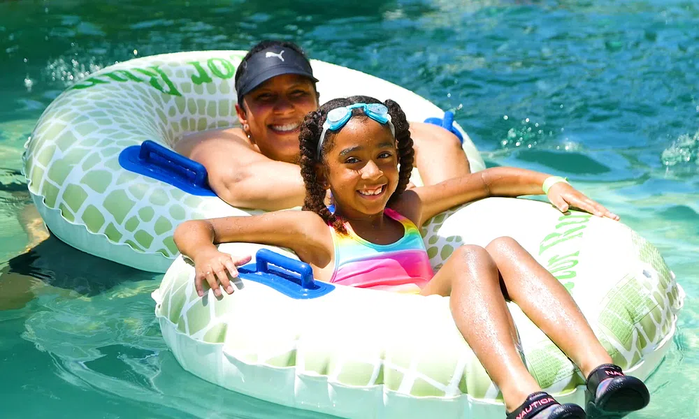 Smiling woman and girl in colorful swimsuit enjoying a sunny day on inflatable tubes in clear water.