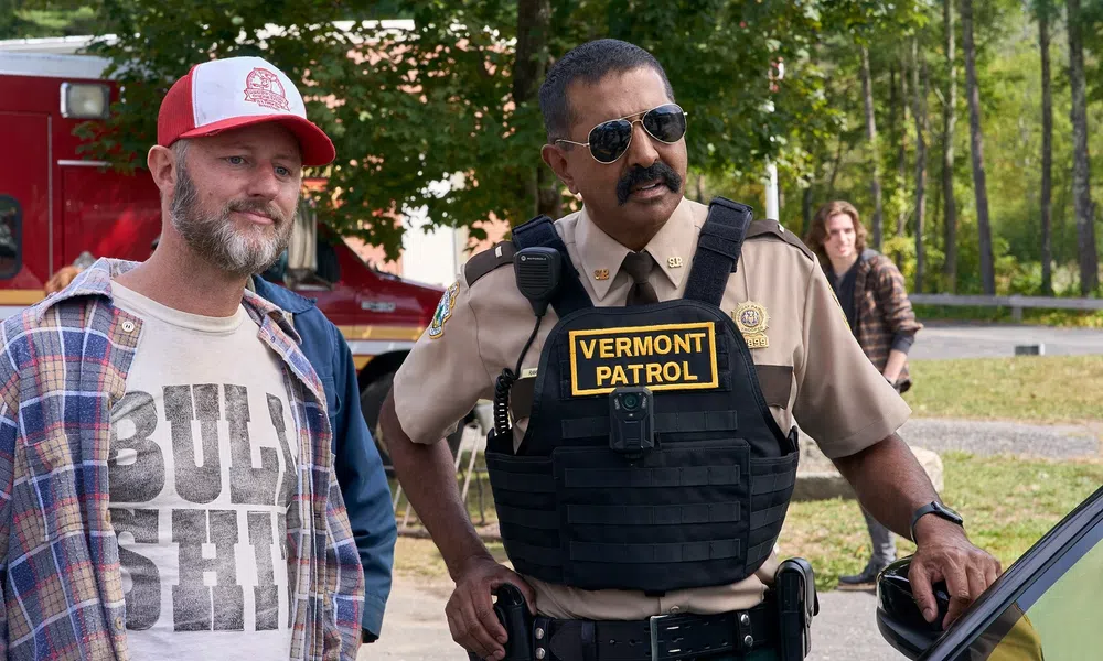 Vermont patrol officer in uniform speaking with a casually dressed man outdoors near an emergency vehicle.