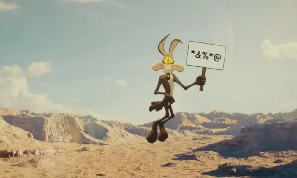 Cartoon coyote holds a sign with symbols in a desert canyon landscape under a clear sky.