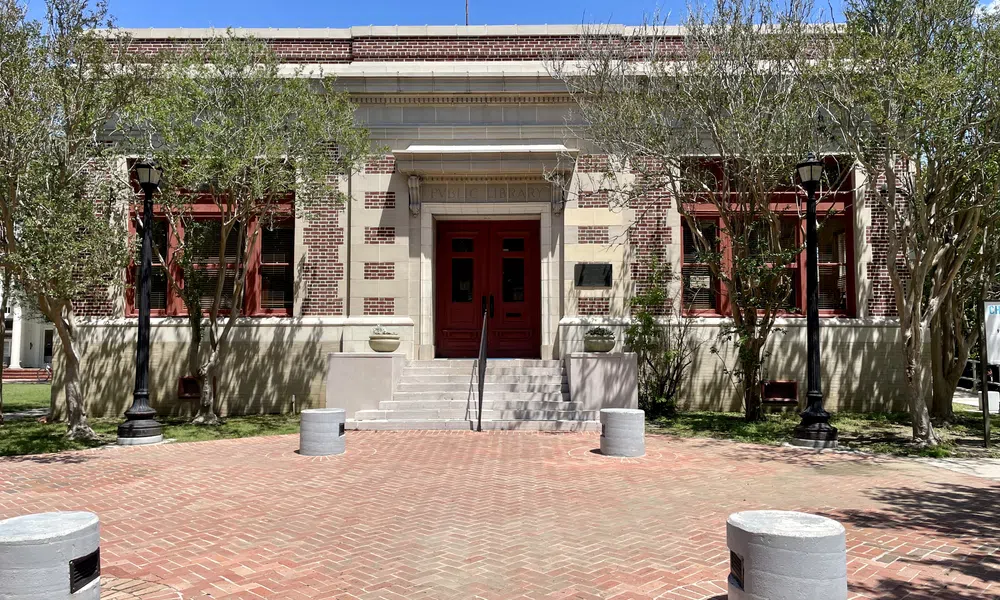 Brick building with red doors and windows, flanked by trees and black street lamps under a clear blue sky.