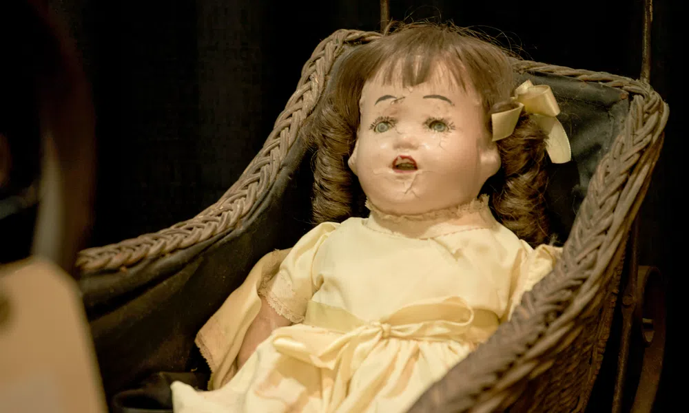 Vintage damaged doll with curly hair in a pale yellow dress sitting in a woven basket cradle.