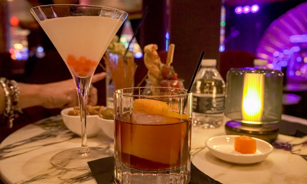 Cocktails served on a marble table with dim lighting and a water bottle in a cozy bar setting.