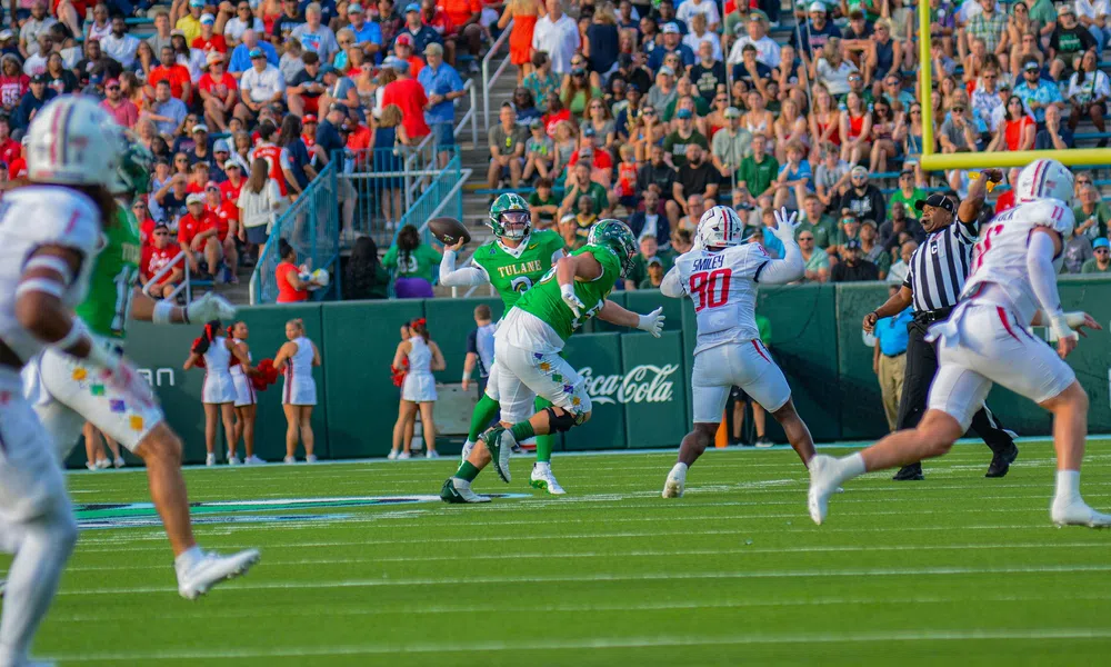 Tulane quarterback prepares to throw under pressure from defenders with crowd and cheerleaders in background