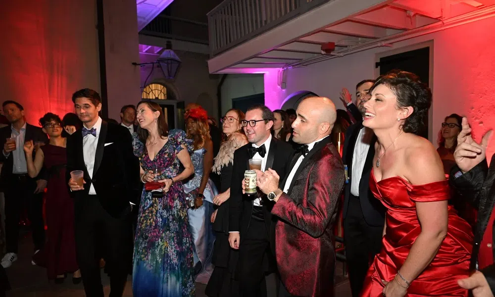 Guests dressed in formal attire enjoy a lively evening party with colorful lighting in an elegant indoor venue.