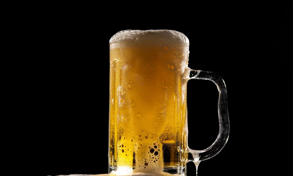 Cold beer mug filled with golden lager and frothy foam against a black background