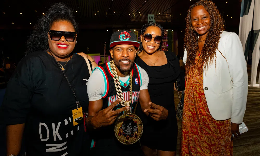 Group of four diverse people smiling at a social event with colorful lighting and casual attire.