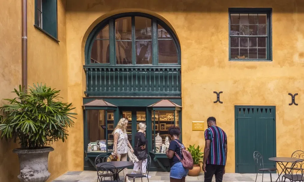 People walking and browsing outside a mustard-yellow building with green framed windows and outdoor tables.