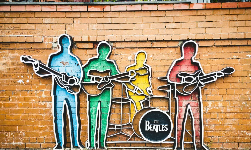 Colorful Beatles band silhouettes mural on brick wall with instruments and drum featuring their band name.