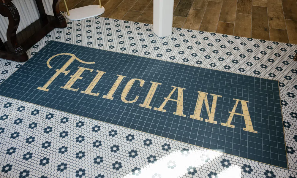 Tiled floor featuring a dark blue rectangular center with gold letters spelling FELICIANA surrounded by hexagonal white and blue tiles.