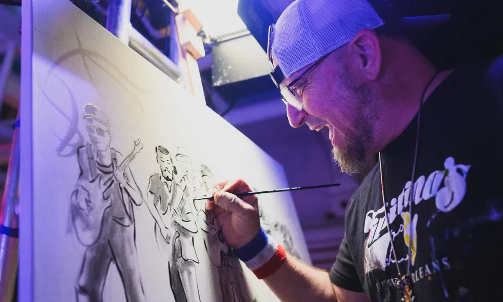 Artist in cap painting a monochrome group portrait on canvas in a studio with focused expression