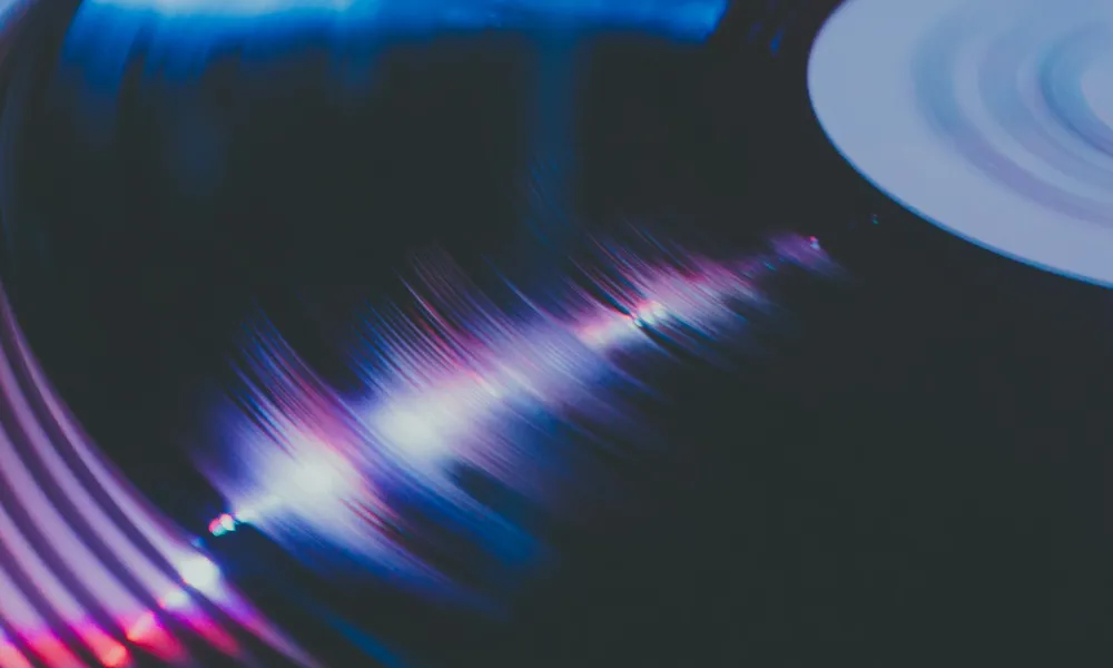 Close-up of a vinyl record spinning with colorful light reflections on its grooves in a dark setting