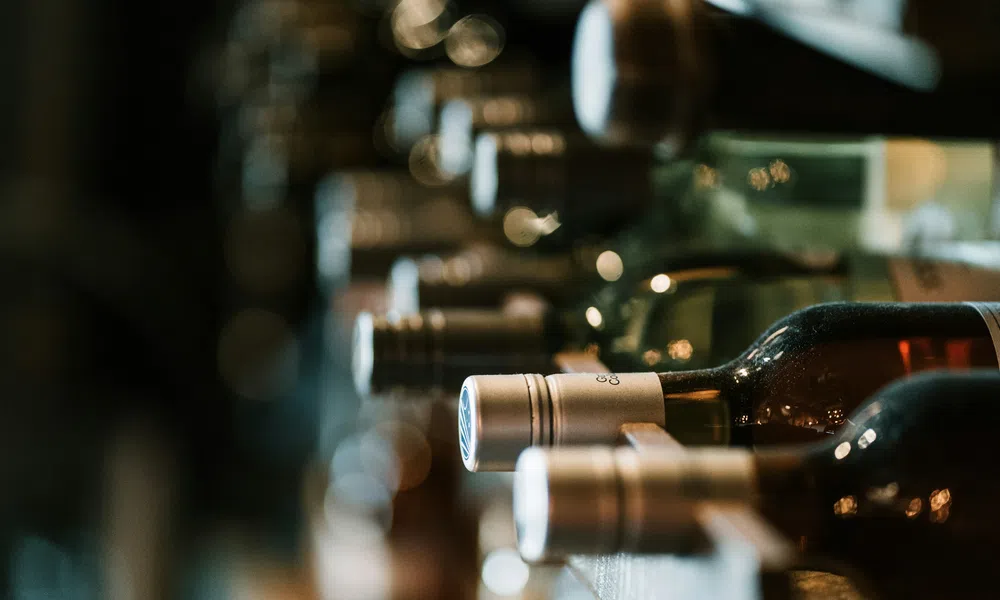 Close-up of wine bottles stacked horizontally on a wooden rack with dim lighting in a cellar or bar.