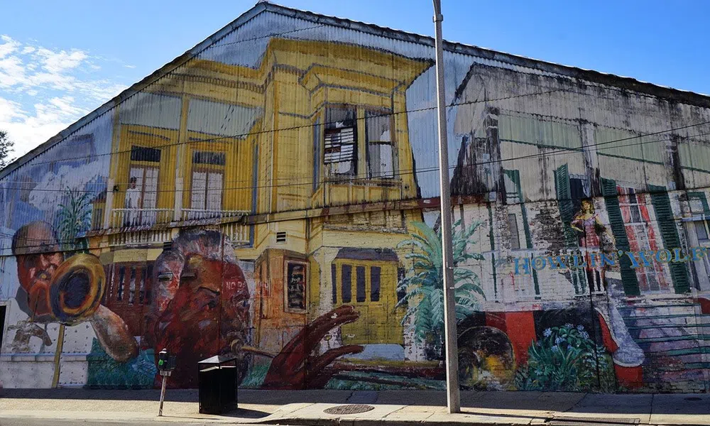Colorful mural on urban street wall featuring musical instruments, people, and yellow building under clear sky.