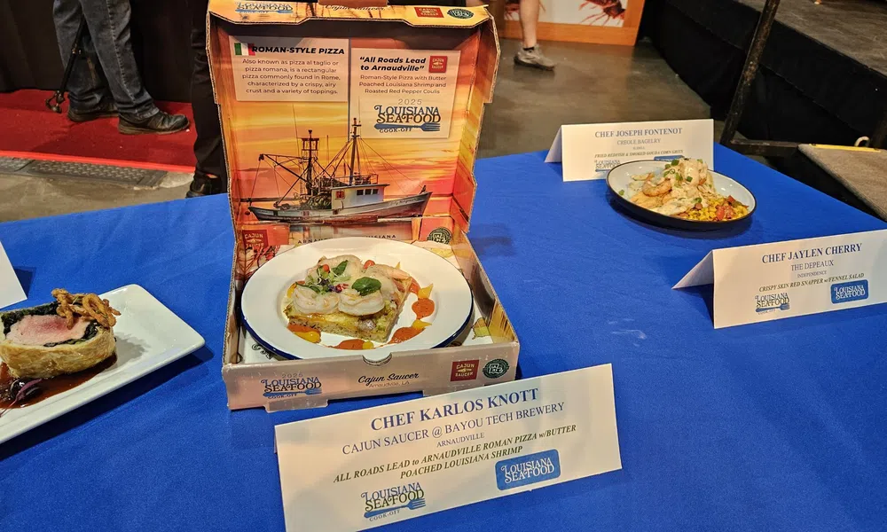 Gourmet seafood dishes displayed on a blue tablecloth with chef name cards at Louisiana Seafood event.