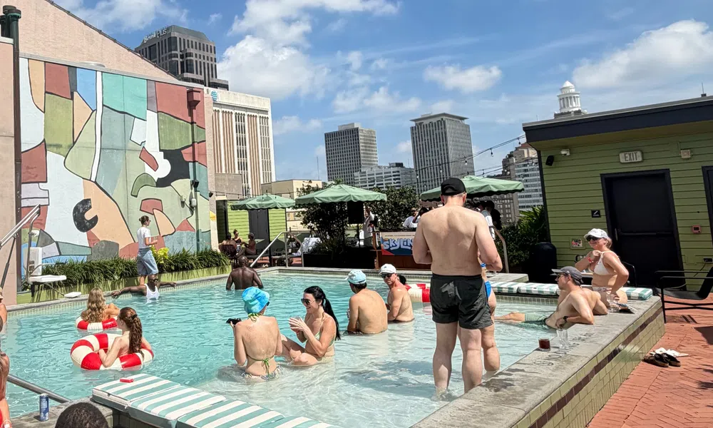 People relaxing and socializing in a rooftop pool with city skyline and colorful mural background on a sunny day.