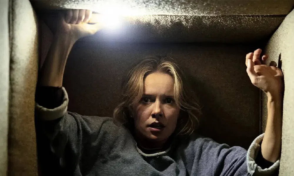 Woman trapped in a small dark space holding a bright flashlight above her head, looking fearful and tense.