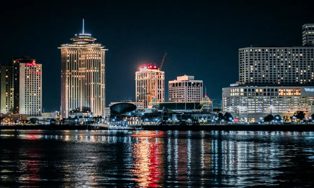 Nighttime city skyline with illuminated tall buildings reflecting on calm river water.