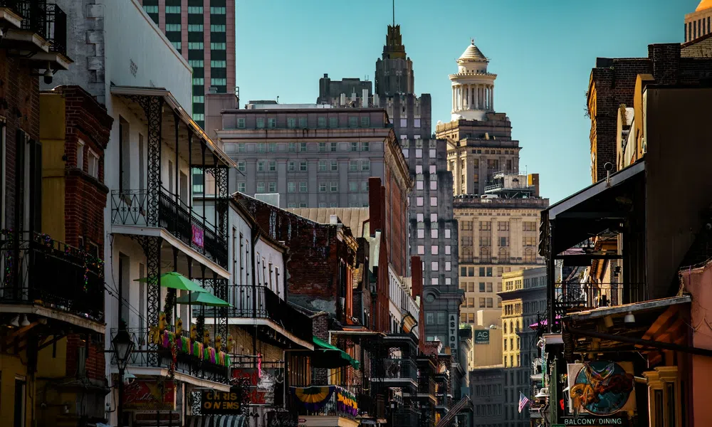 Historic New Orleans street with balconies, colorful decorations, and city skyline in the background under blue sky.