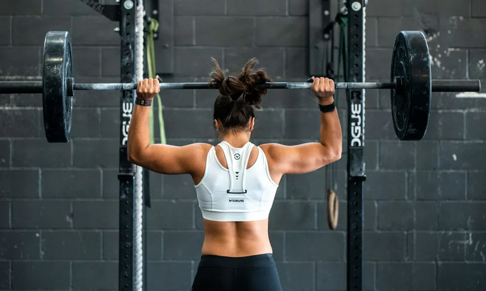 Woman lifting a heavy barbell overhead in a gym with a black brick wall background