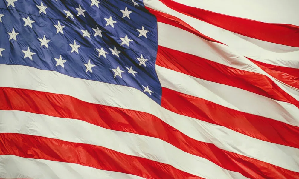 Waving American flag with red and white stripes and white stars on a blue field against sky.