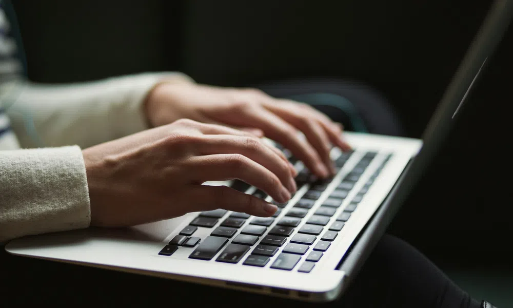Close-up of hands typing on a laptop keyboard in a dimly lit environment with focused activity.