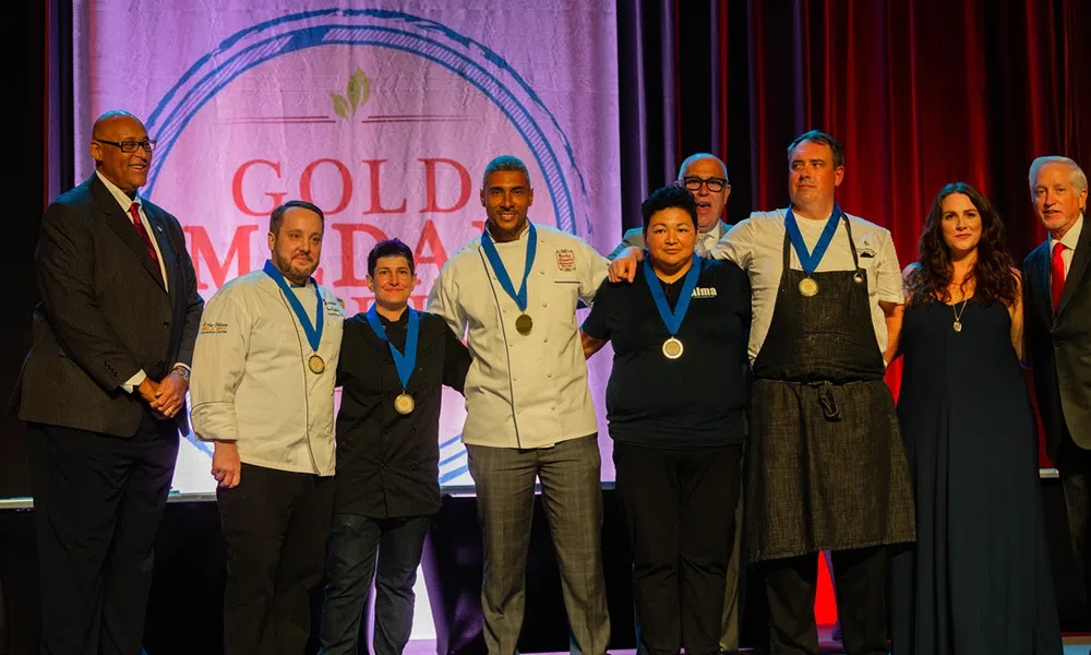 Group of chefs and award recipients wearing medals standing on stage at the Gold Medal event.