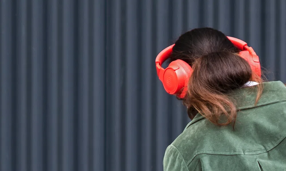Woman with brown hair wearing a green jacket and bright red over-ear headphones against a dark background