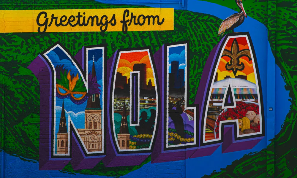 Colorful mural with Greetings from NOLA letters featuring New Orleans iconic landmarks and a pelican on top