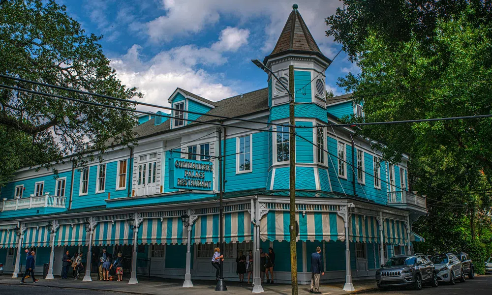 Historic turquoise and white two-story restaurant with striped awnings and pointed turret under a blue sky.