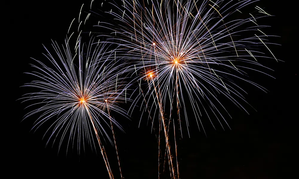 Bright white and orange fireworks bursting against a dark night sky creating a festive display