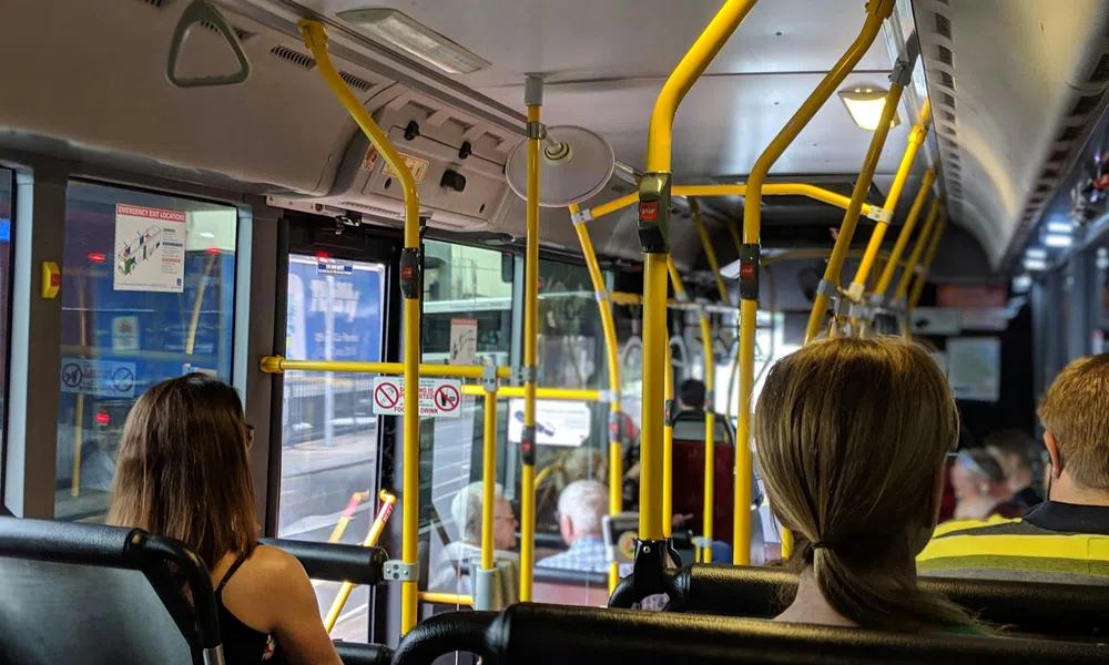 Passengers seated inside a city bus with yellow handrails and windows showing an urban street outside.