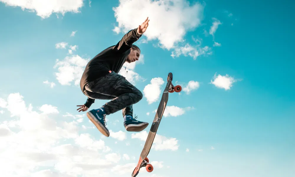 Person performing a high jump trick with a skateboard in mid-air against a blue sky with clouds.