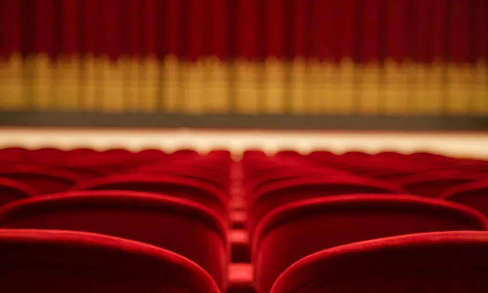 Empty red theater seats facing a closed stage curtain with golden accents under warm lighting.